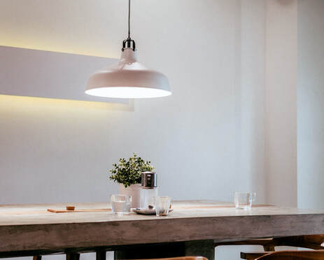 A white pendant light shining onto a wooden dining table
