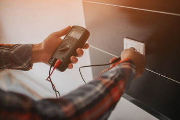 Electrician testing an electrical current using a meter box touching a power point.